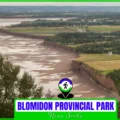 Panoramic aerial view of the towering red sandstone cliffs and the Minas Basin at low tide in Blomidon Provincial Park, Nova Scotia, showing the expansive mudflats, lush green farmland, and distant views of the Bay of Fundy.