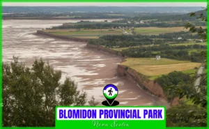 Panoramic aerial view of the towering red sandstone cliffs and the Minas Basin at low tide in Blomidon Provincial Park, Nova Scotia, showing the expansive mudflats, lush green farmland, and distant views of the Bay of Fundy.