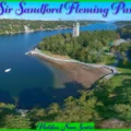 An aerial panoramic view of Sir Sandford Fleming Park in Halifax, Nova Scotia, featuring the historic Dingle Tower, the paved waterfront seawall walkway, and lush green parkland bordering the blue waters of the Northwest Arm.