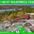 Vibrant autumn foliage in shades of orange and red surrounding the calm waters of Pot Lake on The Bluff Wilderness Hiking Trail in Timberlea, Nova Scotia, under a clear blue sky.